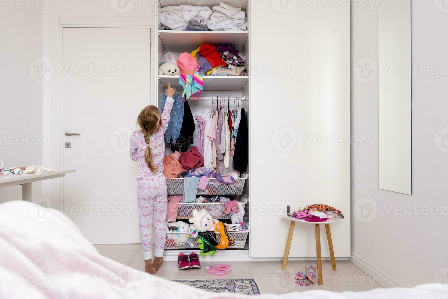 peu fille dans rose rose pyjamas bloque des choses dans le placard, désordre dans le pièce photo