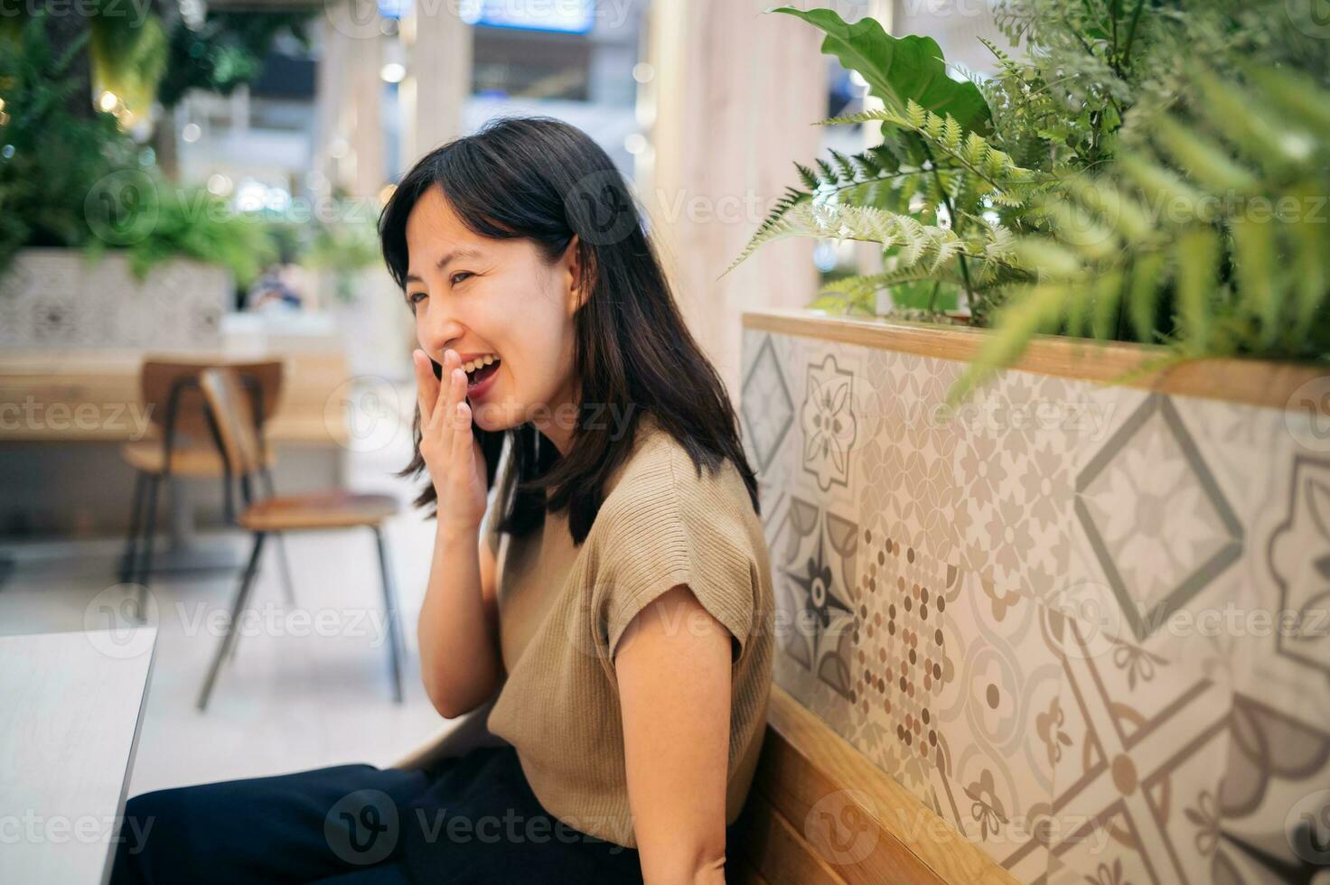 en riant magnifique asiatique femme séance dans cafétéria à achats centre commercial. photo