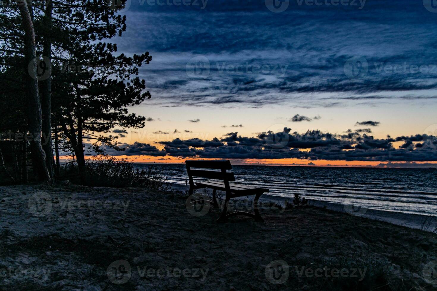 bord de mer paysage avec le coucher du soleil et une solitaire banc permanent sur une dune photo