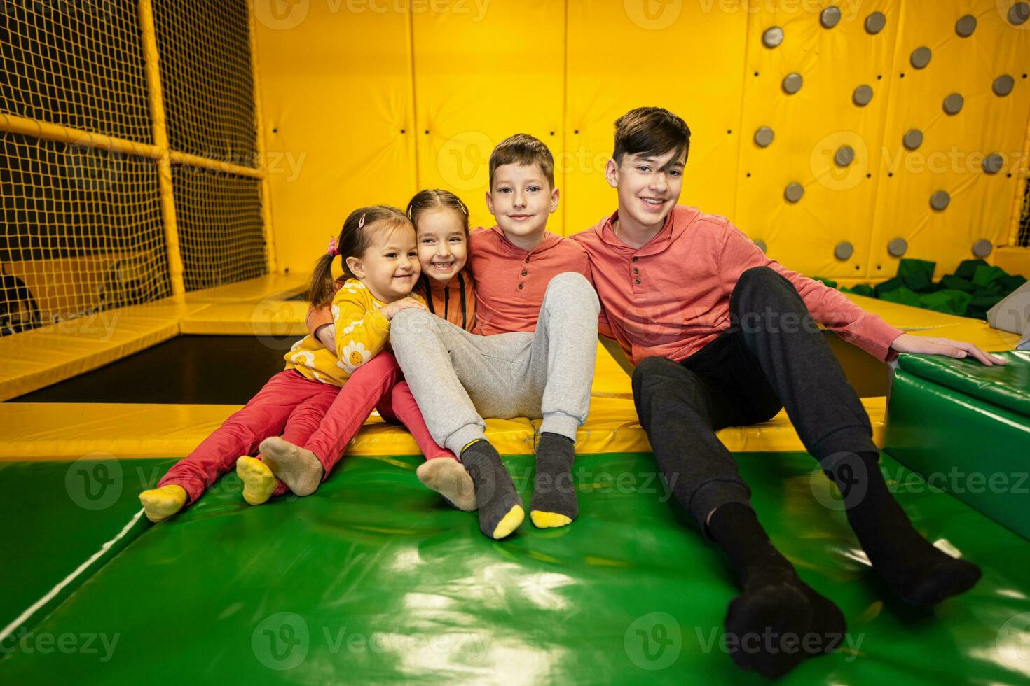 quatre des gamins ensemble asseoir à terrain de jeux parc. sœurs et frères dans actif divertissements. photo