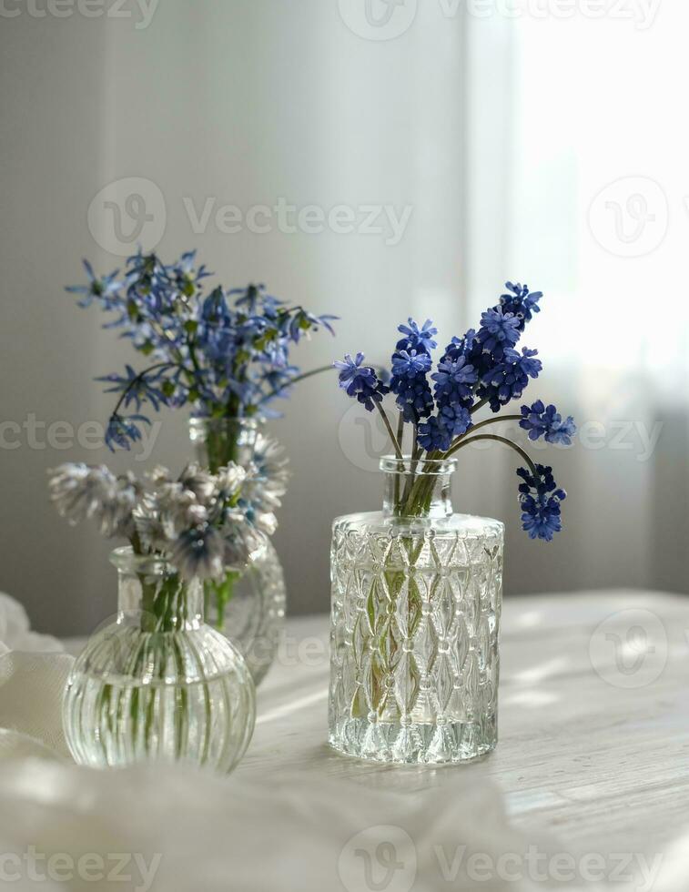 diverses fleurs printanières dans des bouteilles en verre sur une table près de la fenêtre au soleil. printemps nature morte photo