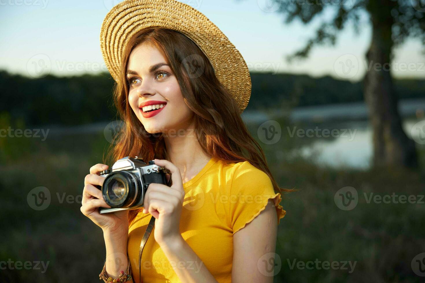 jolie femme avec une caméra dans sa mains sur la nature portant chapeau rouge lèvres sourire regards en haut photo