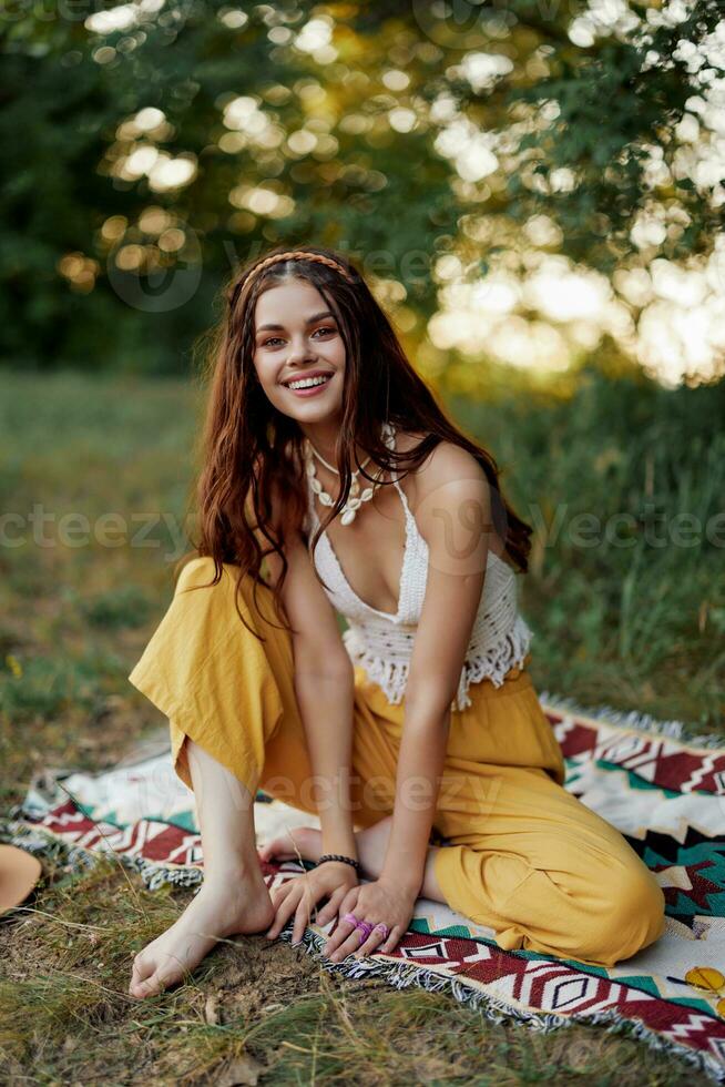 Jeune magnifique hippie femme séance sur le sol dans la nature dans le l'automne dans éco Vêtements dans le le coucher du soleil lumière, une mode de vie de Voyage et harmonie avec le monde photo