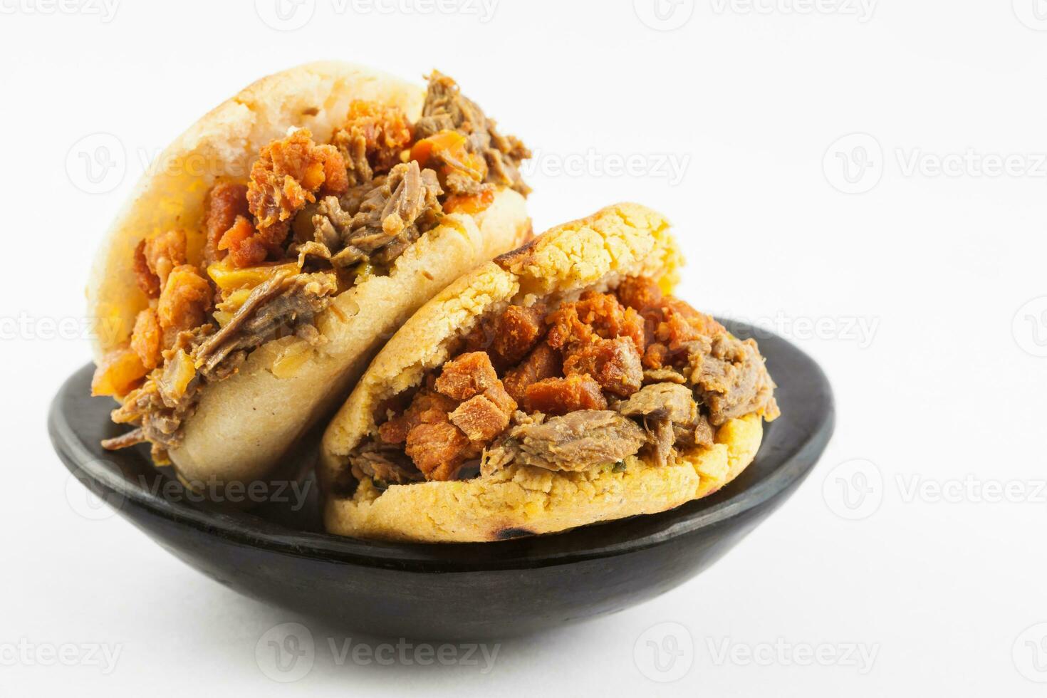 arepas rempli avec déchiqueté du boeuf et porc couenne servi dans une noir céramique plat sur blanc Contexte photo