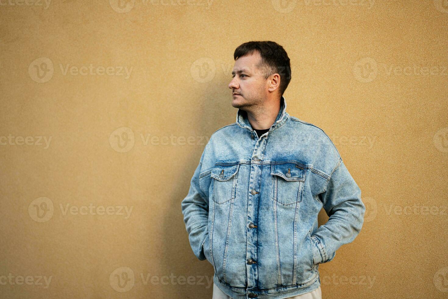 côté portrait de élégant homme dans jeans veste contre Jaune mur. photo