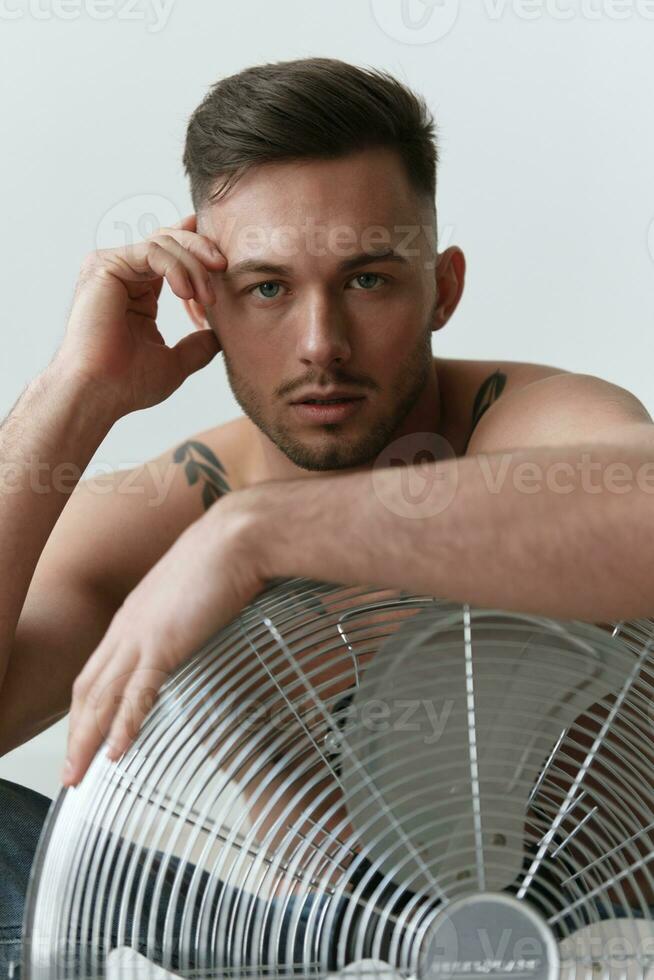 la modélisation instantanés. fermer portrait de attrayant nu Beau homme dans jeans penché sur ventilateur séance sur sol posant dans blanc studio Contexte. mode Hommes tirer concept. copie espace. cool offre photo