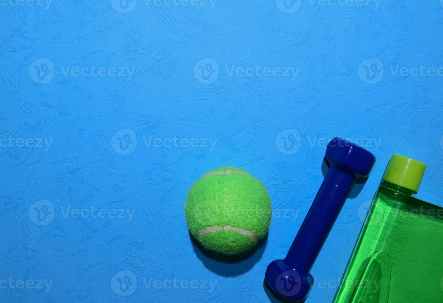 bleu haltère, vert tennis balle, et bouteille indiquant faire des exercices plan sur bleu Contexte. Haut vue avec copie espace pour tout conception. en bonne santé et aptitude concept photo