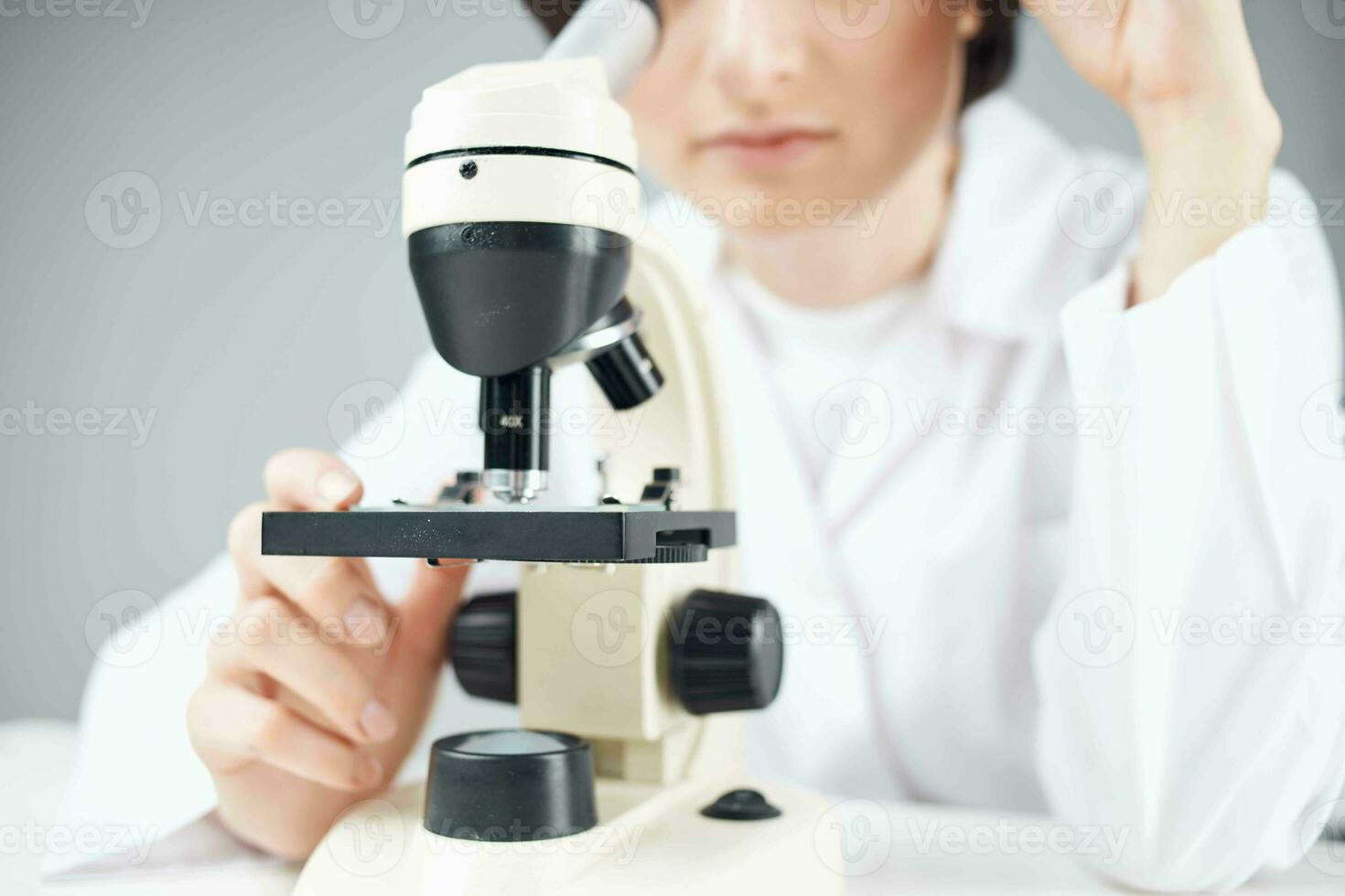une scientifique dans une blanc manteau à la recherche par une microscope fermer laboratoire photo