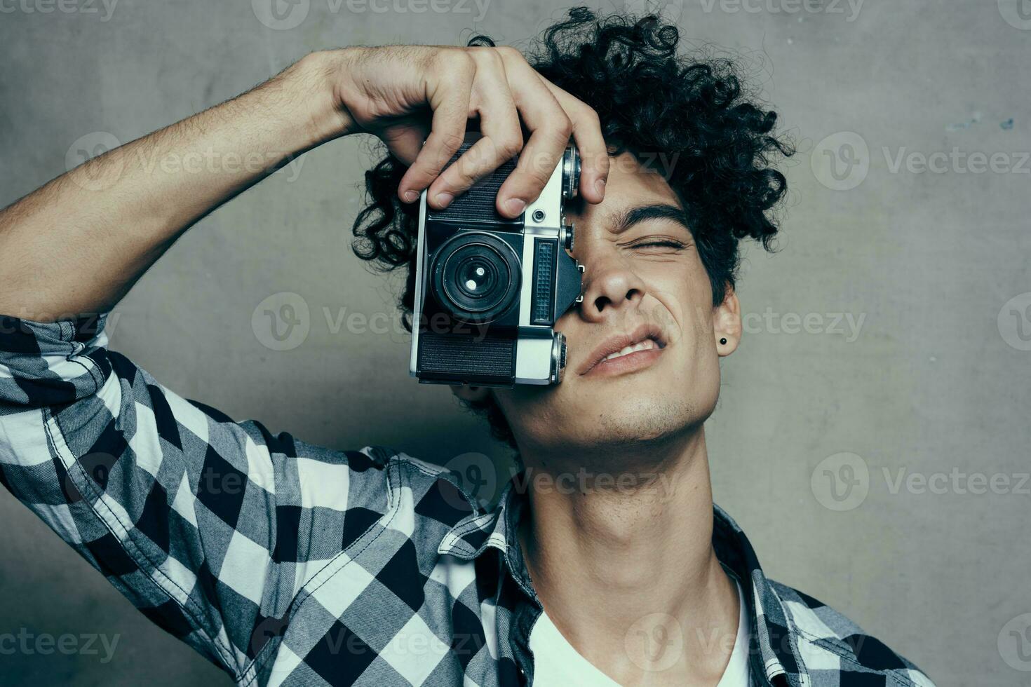 Beau gars avec une caméra près le sien visage et frisé cheveux plaid chemise loisir photographe photo