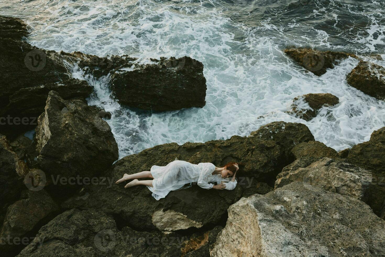 attrayant femme avec longue cheveux mensonge sur rocheux côte avec des fissures sur rocheux surface inchangé photo