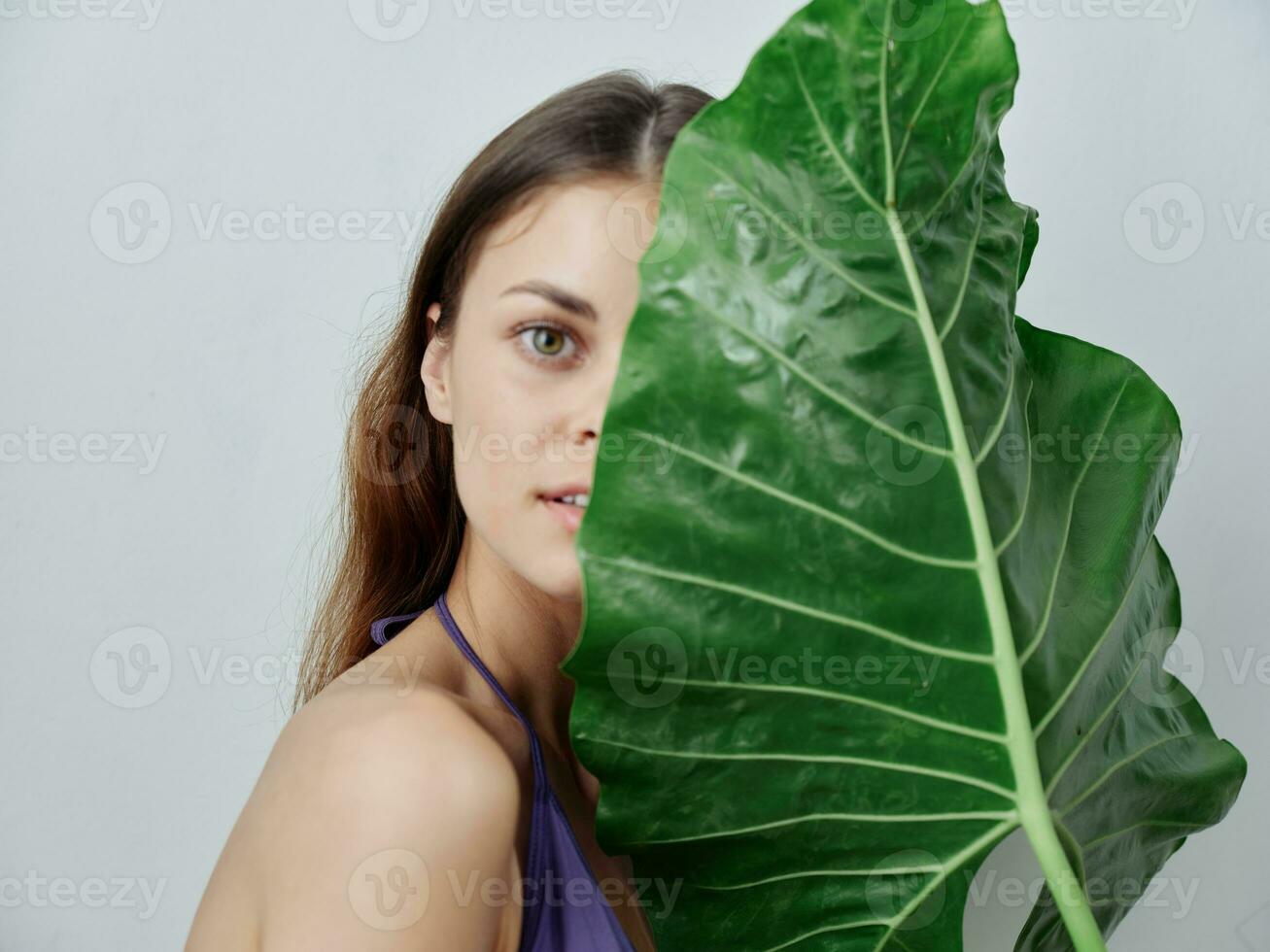 jolie femme couvertures moitié de sa visage avec vert feuille maillot de bain tondu vue photo