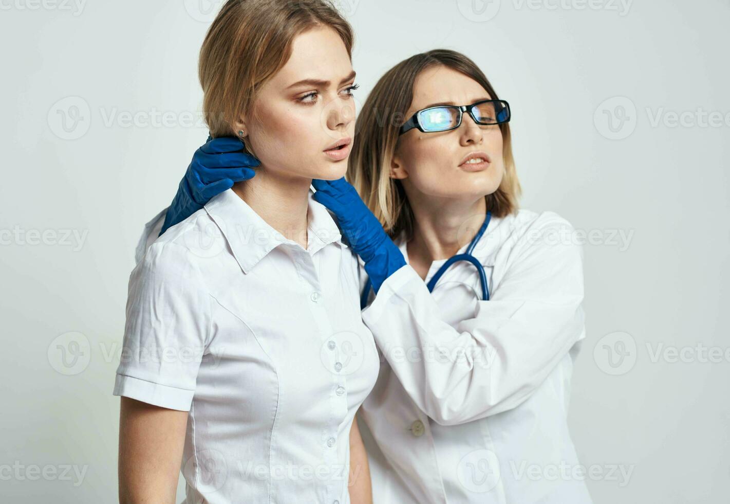 une infirmière dans bleu gants examine une patient dans une blanc T-shirt sur une lumière Contexte photo