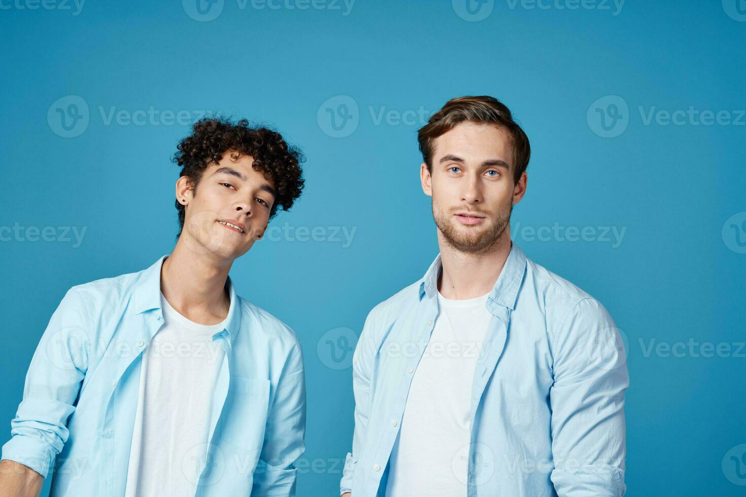 deux copains dans identique chemises et une T-shirt faire des gestes avec leur mains sur une bleu Contexte photo