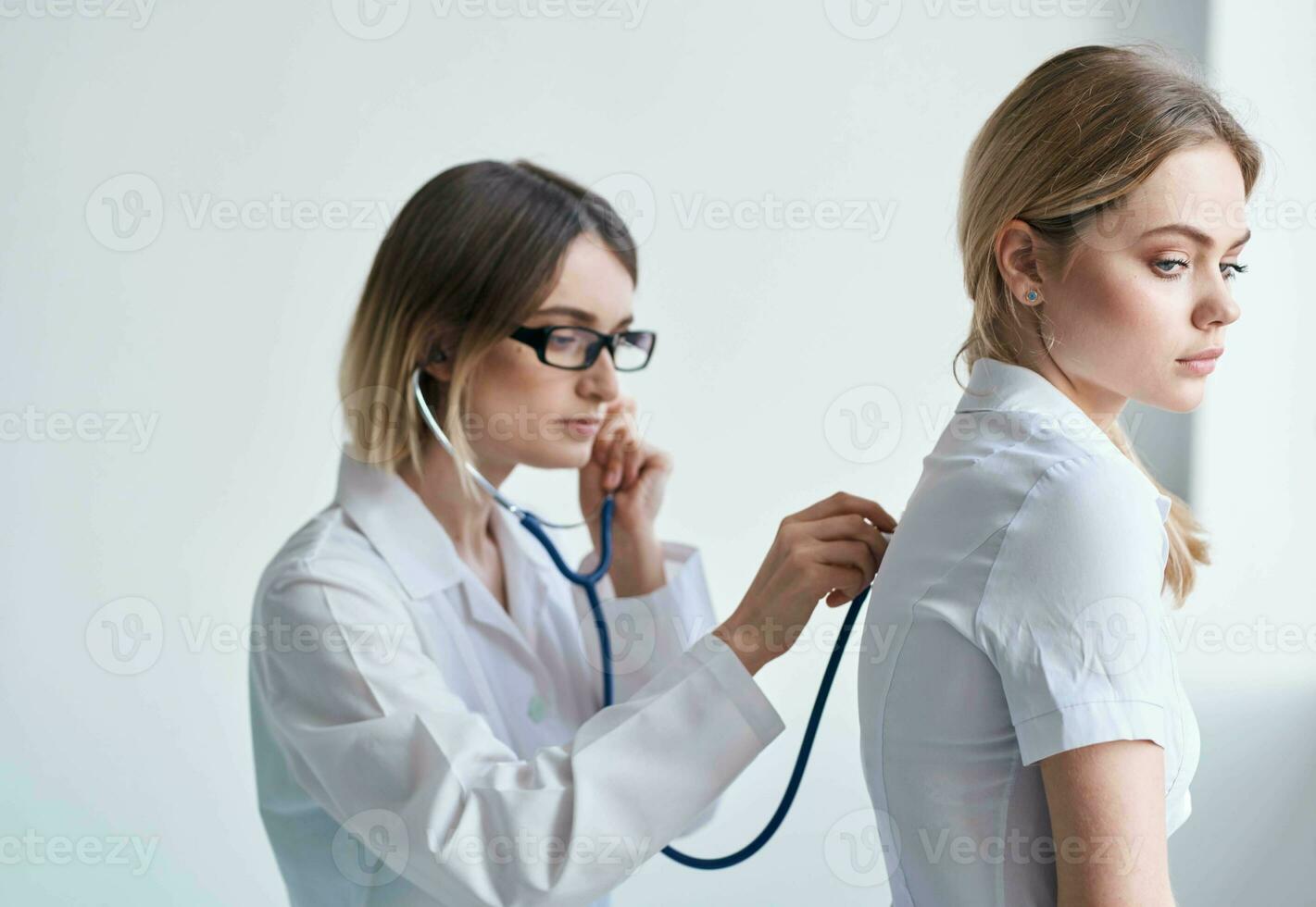 médecin dans une médical robe avec une stéthoscope examine une patient sur une lumière Contexte photo