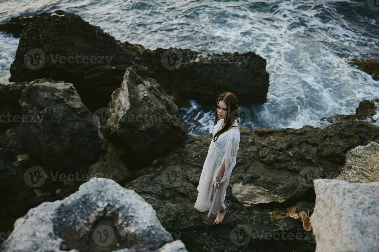 une femme dans une blanc robe des stands sur le des pierres par le océan Haut vue photo