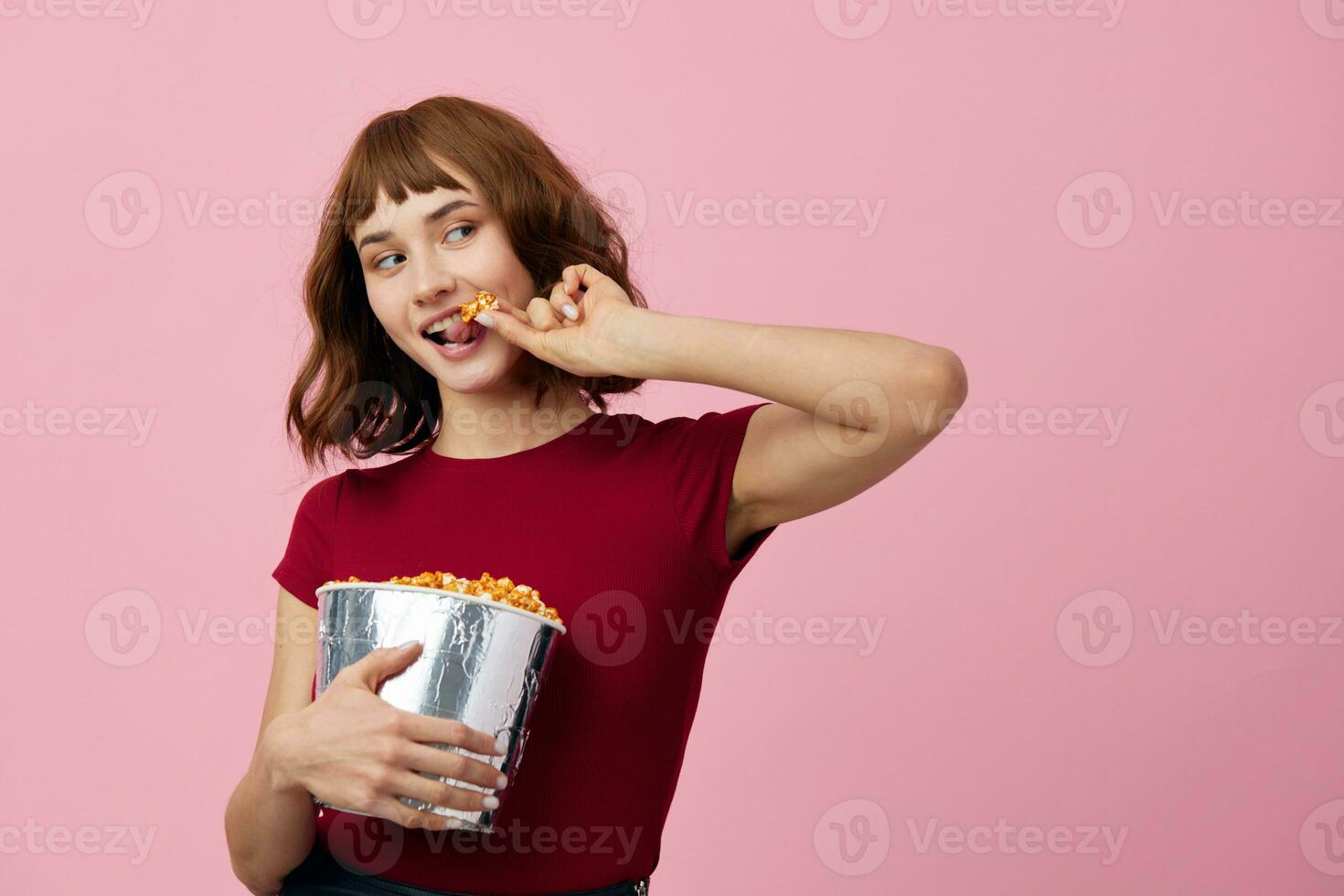 souriant de bonne humeur jolie mignonne roux Dame dans rouge chemise avec pop corn prêt à regarder film posant isolé sur plus de rose studio Contexte. copie espace bannière. mode cinéma concept. divertissement offre photo