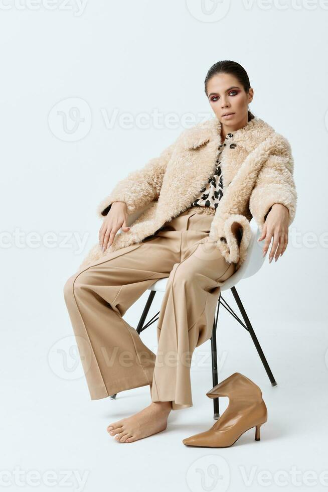 glamour femme séance sur une chaise dans une blanc fourrure manteau à la mode vêtements posant photo