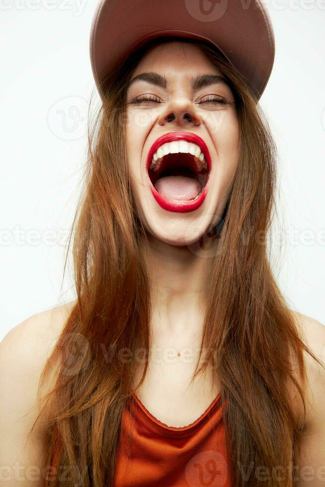 portrait de une femme dans une casquette ouvert bouche langue fermé yeux amusement rouge lèvres photo