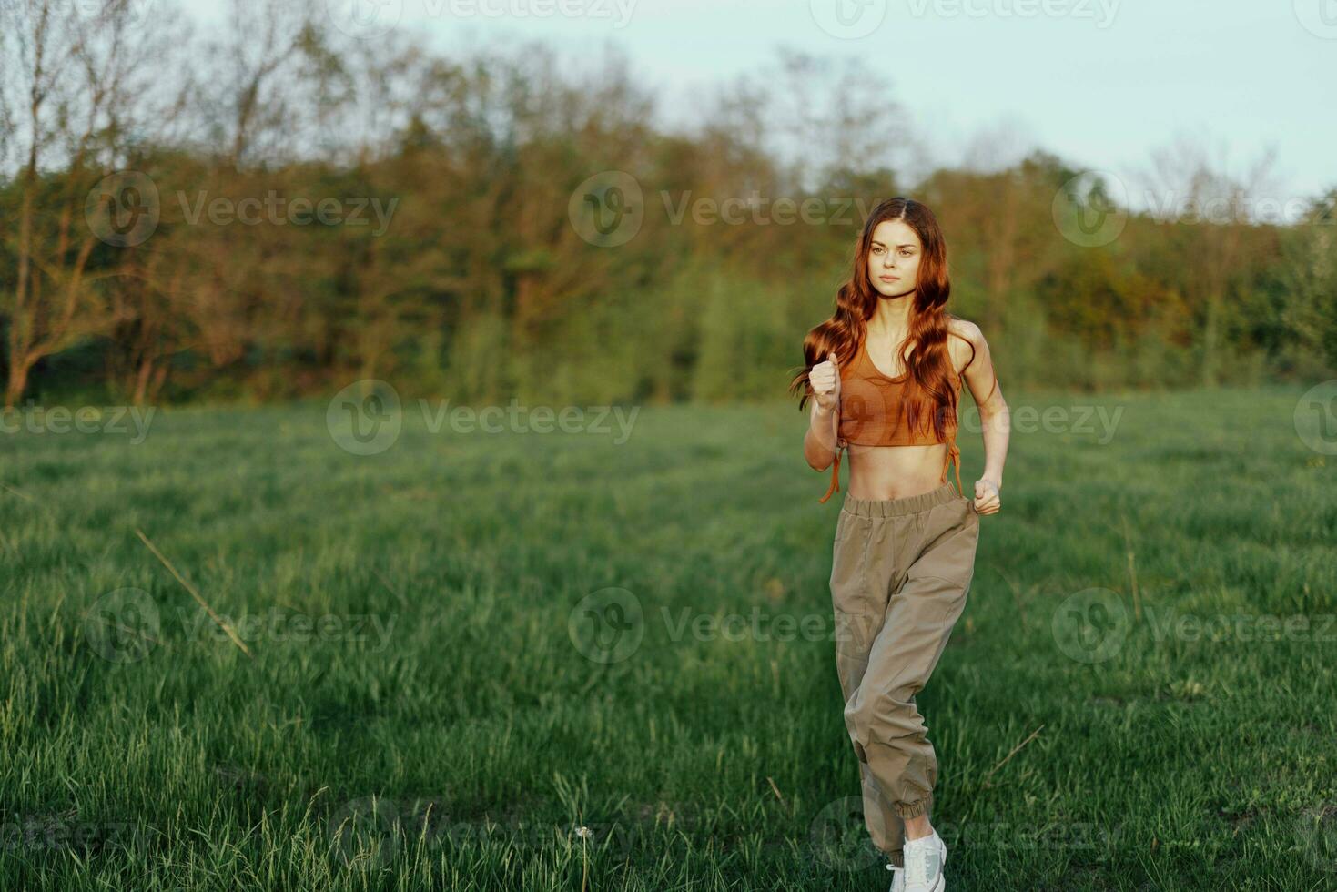 une content athlétique femme est le jogging et souriant dans la nature dans le parc, été le coucher du soleil lumière photo