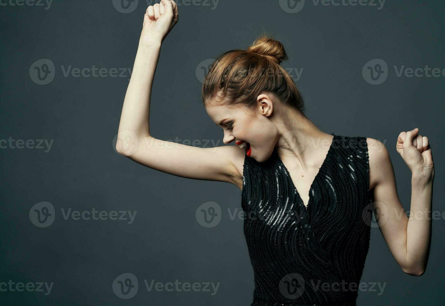 élégant Dame dans une noir robe sur une gris Contexte gestes avec sa mains émotions surprise joie photo