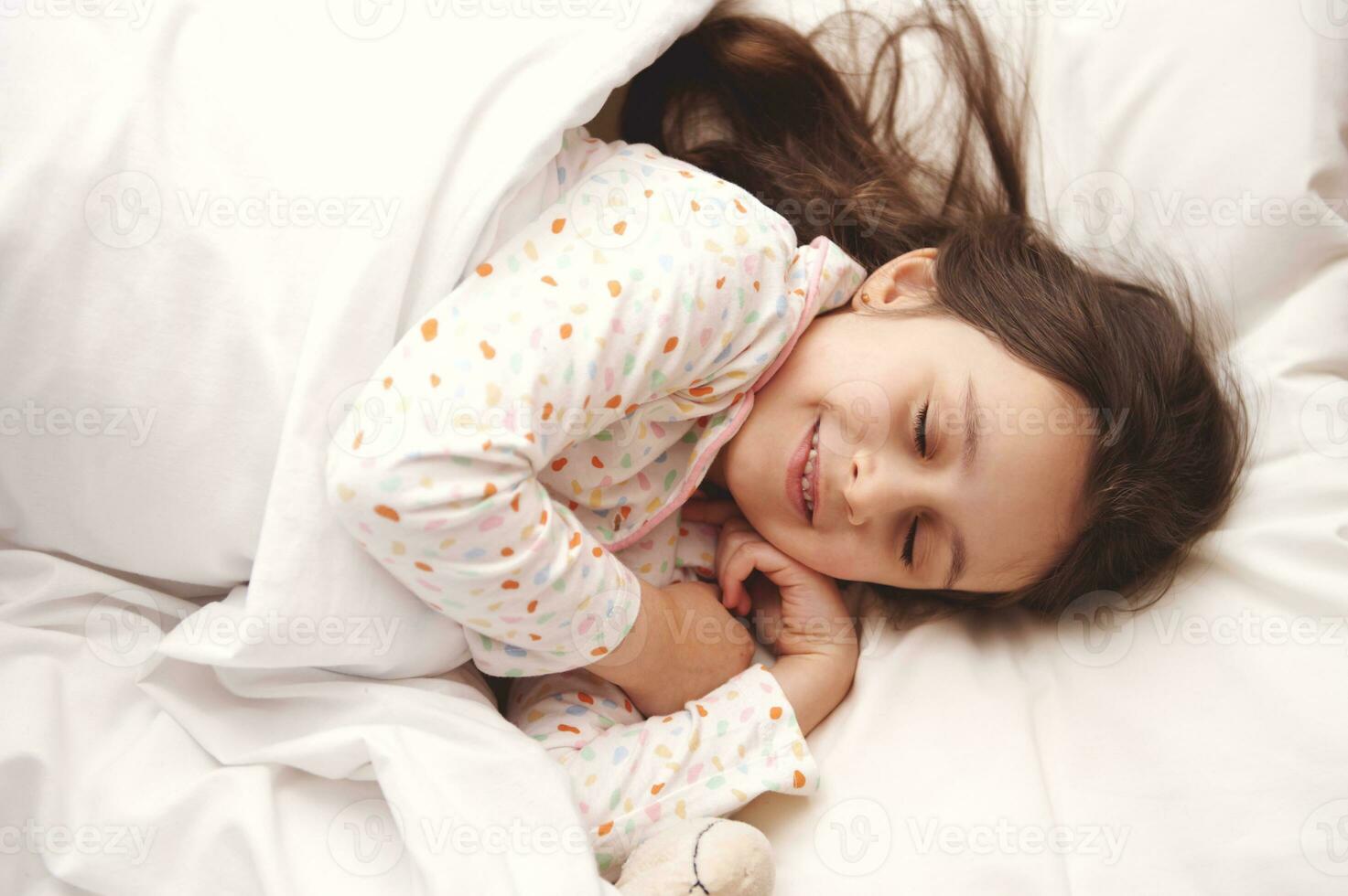 vue de au dessus de une caucasien magnifique peu enfant fille dans blanc pyjamas, prise une sieste dans une blanc ensoleillé chambre photo