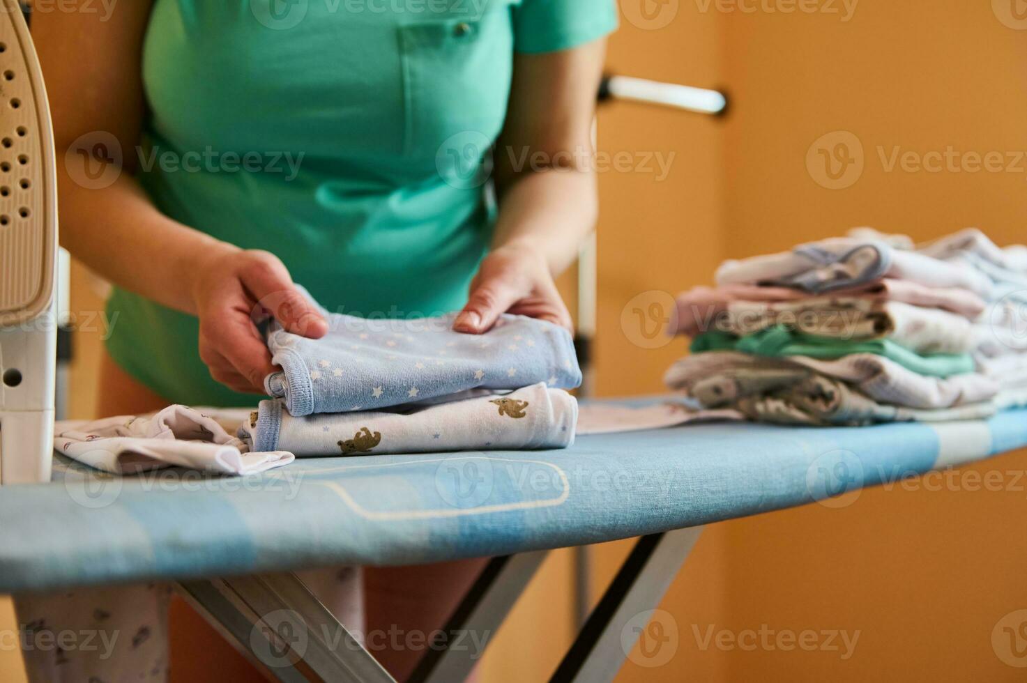 fermer de femme enceinte mère organiser nettoyer blanchi et repassé vêtements pour le futur nouveau née bébé sur repassage planche photo