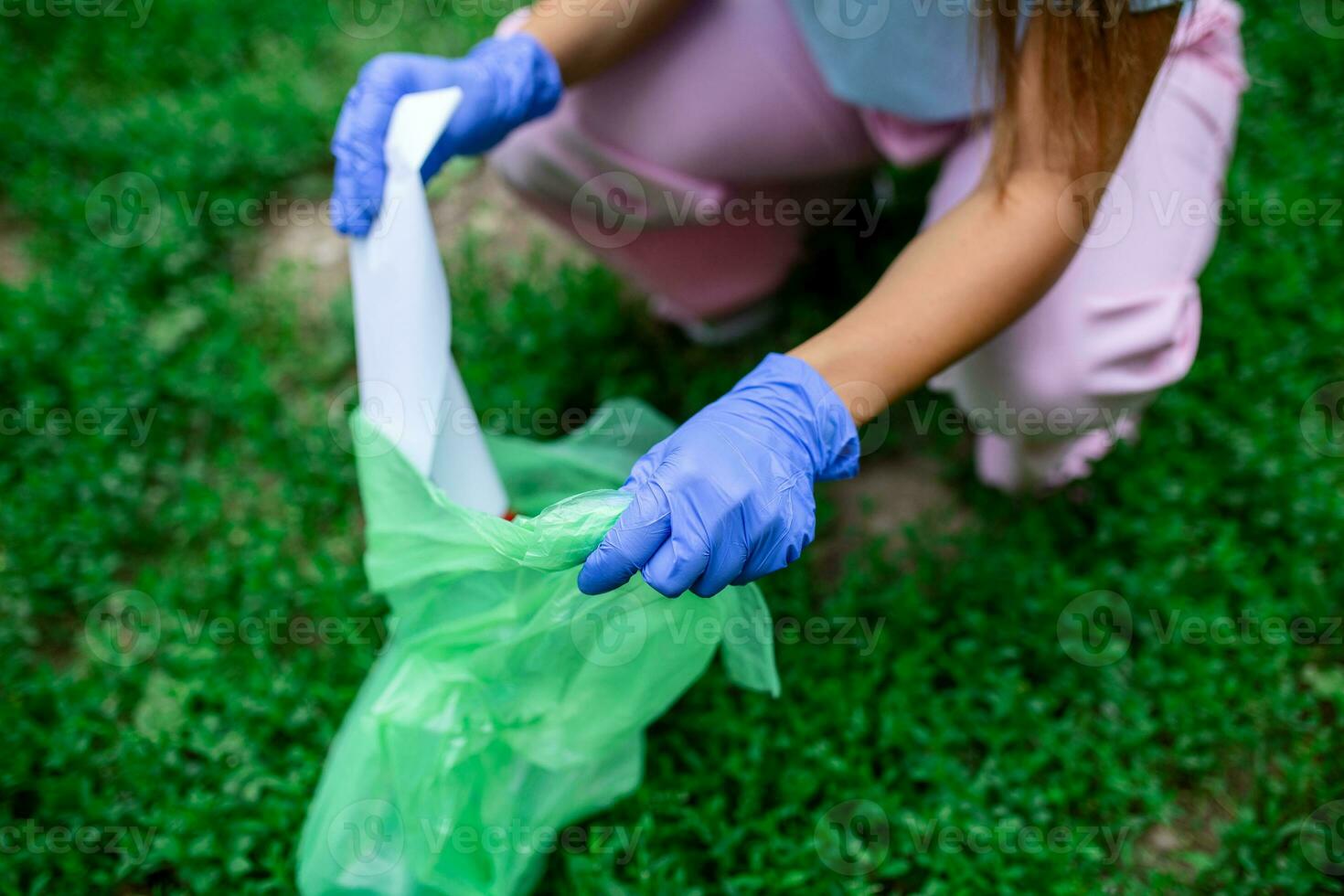 main de femme cueillette en haut papier dans des ordures Sacs tandis que nettoyage zone dans parc. faire du bénévolat, charité, personnes, écologie concept. fermer bénévole collecte Plastique poubelle dans forêt. photo