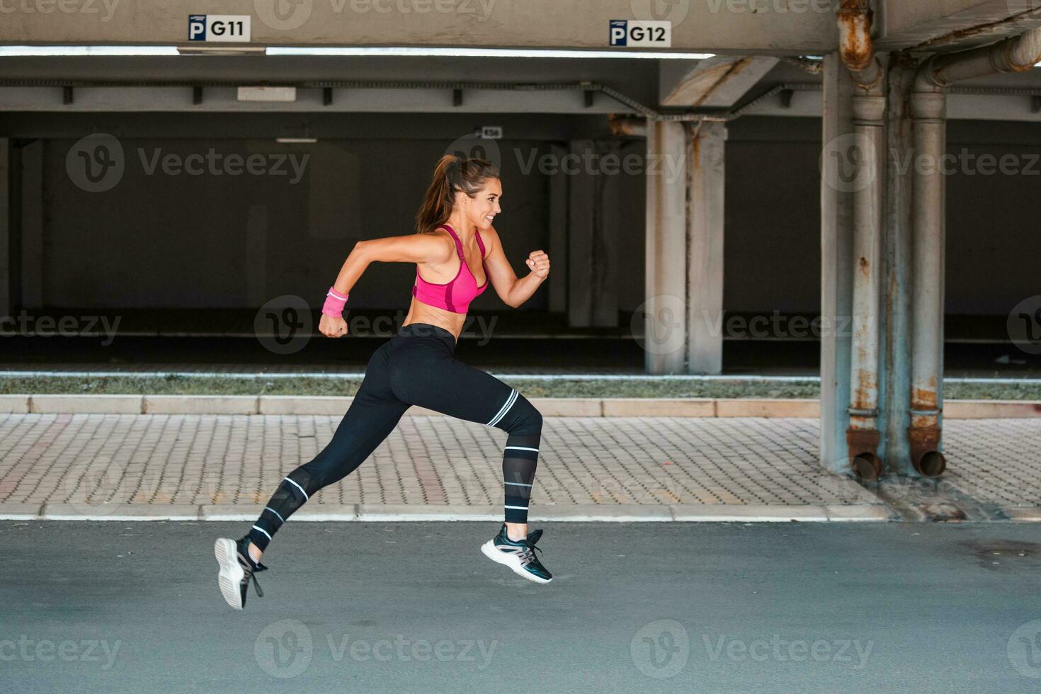 Jeune femme avec en forme corps sauter et fonctionnement contre gris Contexte. femelle modèle dans tenue de sport exercice en plein air. photo