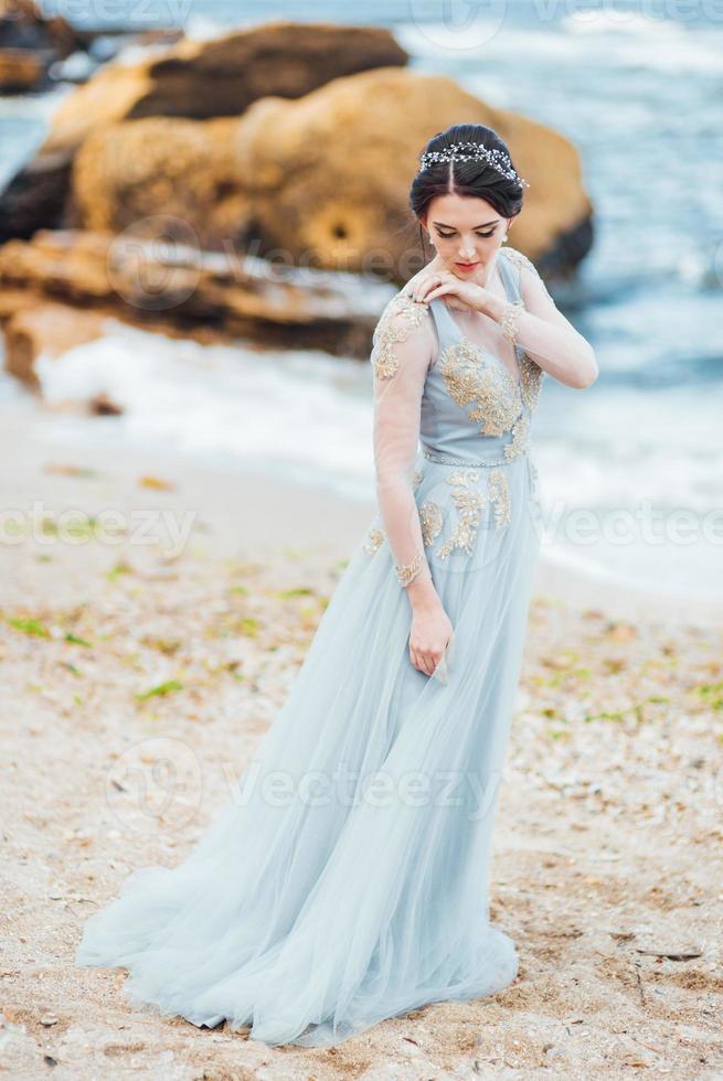 mariée dans une robe de lumière bleue marchant le long de l'océan photo