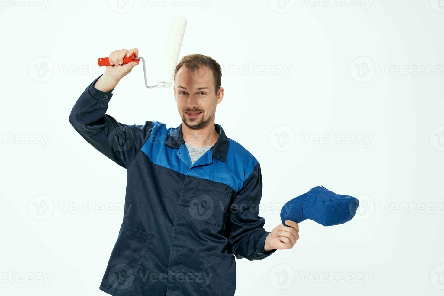 une homme dans une travail uniforme une rouleau pour La peinture des murs dans le sien mains décoration réparation photo