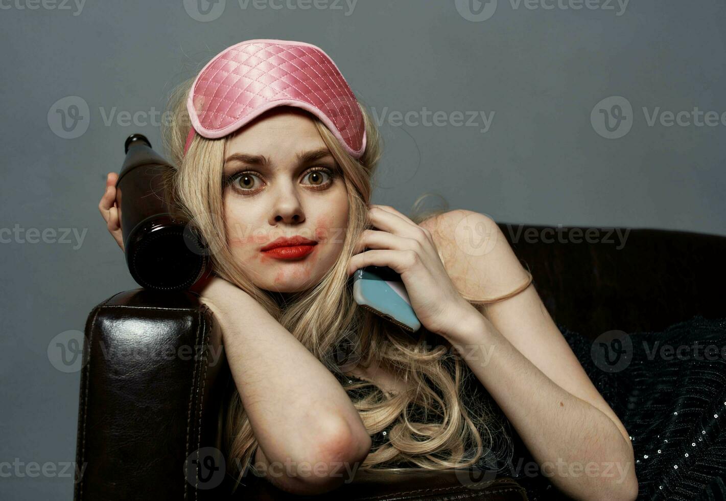 une femme dans une rose masque mensonges sur le canapé avec une bouteille de Bière et une téléphone dans sa main photo