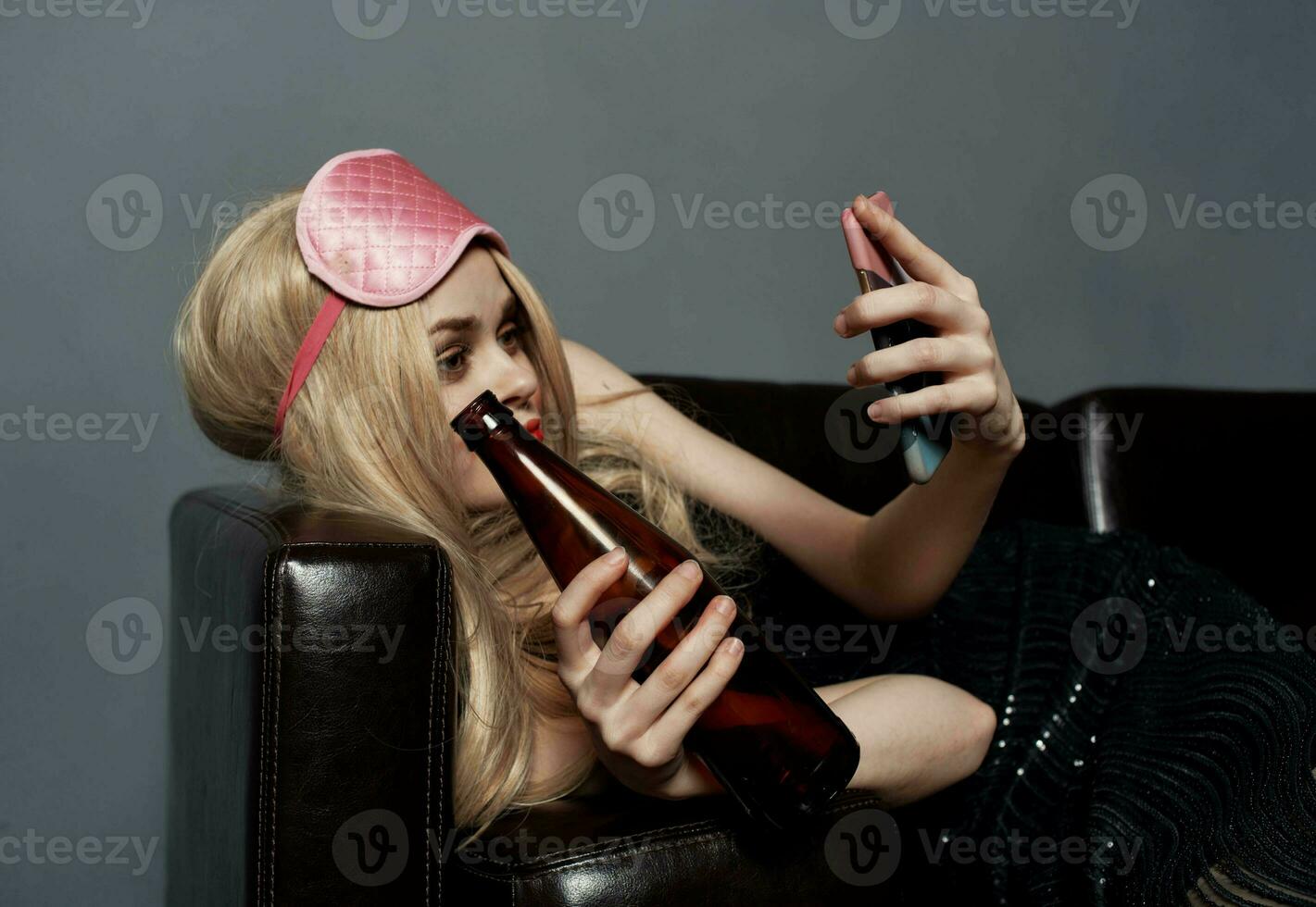 une ivre femme avec une bouteille de Bière regards à une mobile téléphone dans sa main et mensonges sur le canapé photo