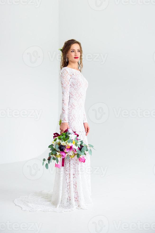 mariée fille joyeuse dans une robe tricotée blanche posant avec un bouquet de fleurs photo