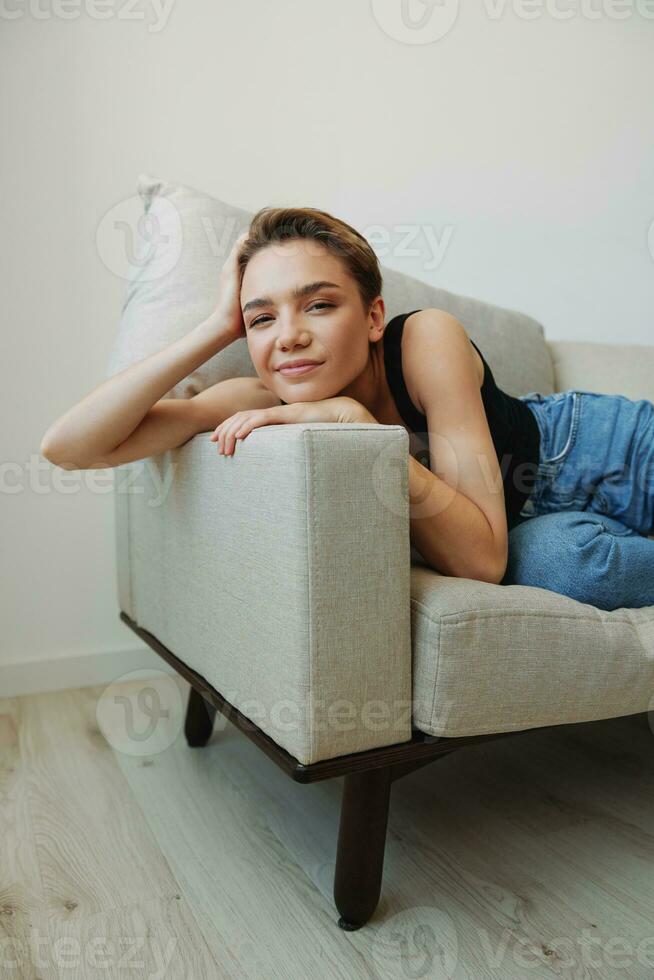 Jeune femme avec court la Coupe de cheveux cheveux ayant amusement à Accueil sur le canapé sourire et bonheur, vacances à maison, Naturel posant sans pour autant filtres, gratuit copie espace photo