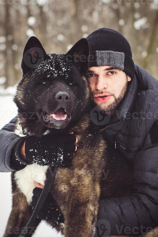 Un homme dans une veste et un bonnet tricoté se promène avec un chien akita américain photo