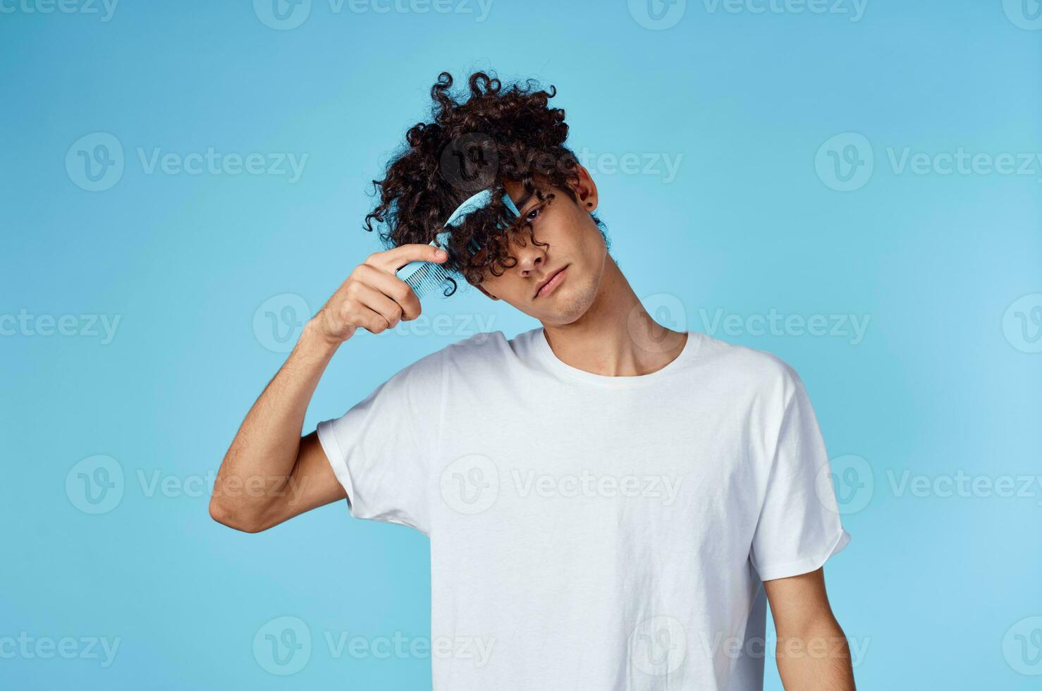 mignonne homme avec frisé cheveux en portant peigne dans main et bleu Contexte tondu vue photo