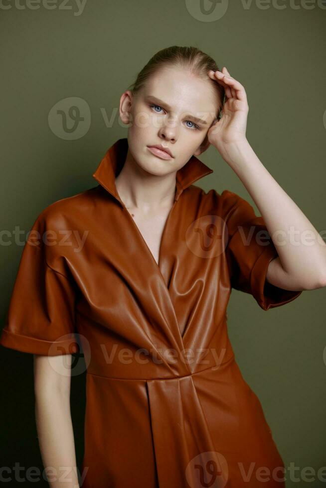 sérieux confiance Jeune blond fille avec queue de cheval dans élégant cuir robe regards à caméra émouvant tête posant isolé pour marché bannière. studio portrait sur vert Contexte. revente concept photo