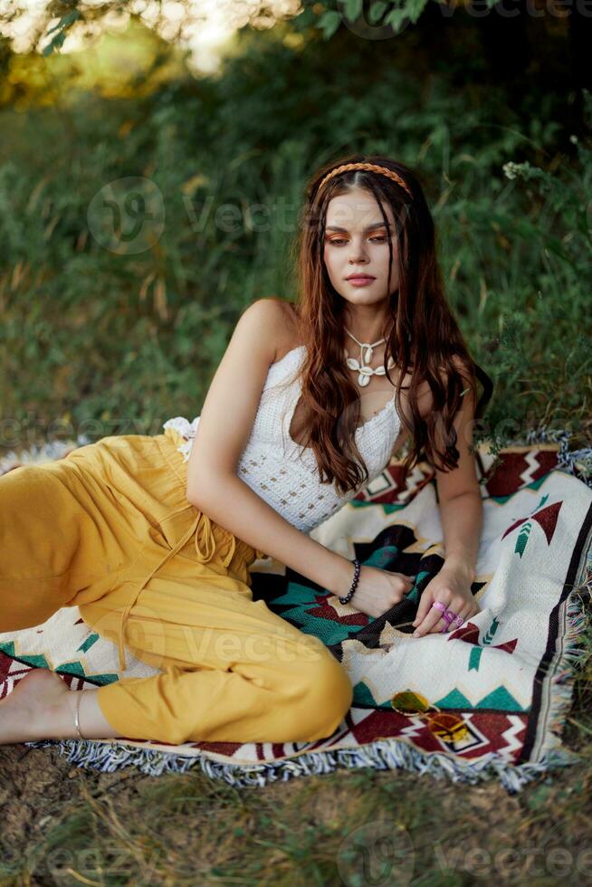 Jeune magnifique hippie femme mensonge sur le sol dans la nature dans le tomber dans éco vêtements dans Jaune un pantalon dans le le coucher du soleil lumière photo