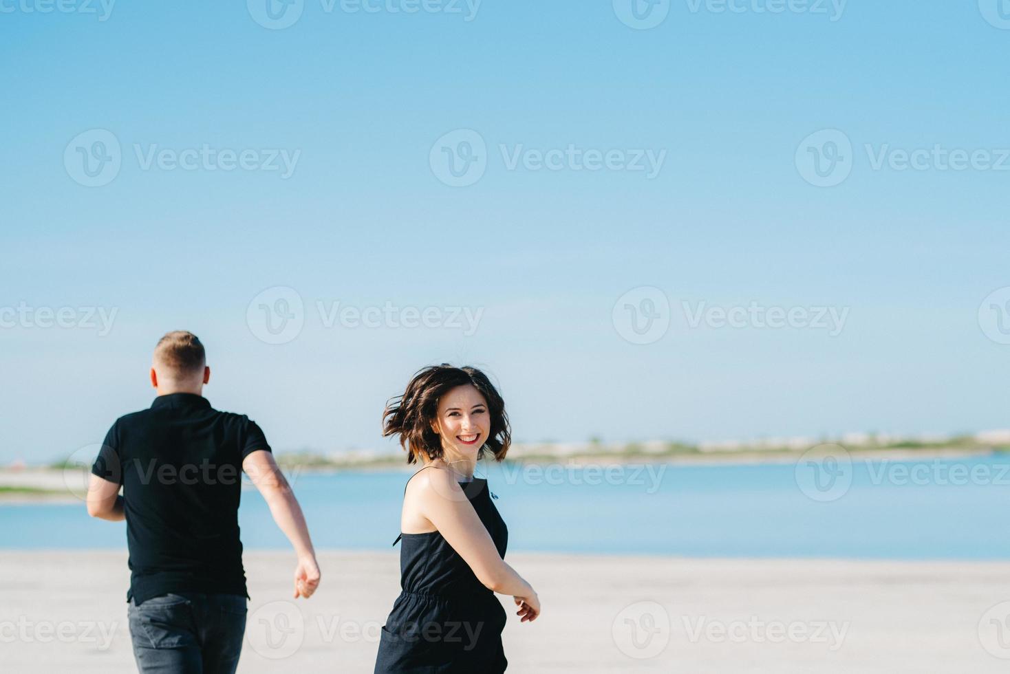 jeune couple un mec avec une fille en vêtements noirs marchent sur le sable blanc photo