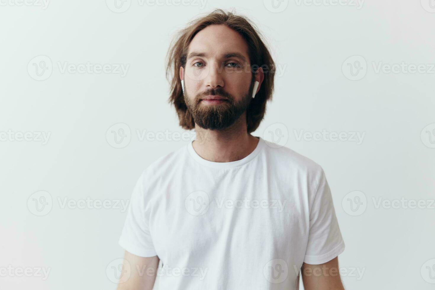 élégant homme dans une blanc T-shirt avec sans fil écouteurs dans le sien oreilles ayant amusement écoute à la musique sourire sur une blanc Contexte mode de vie photo