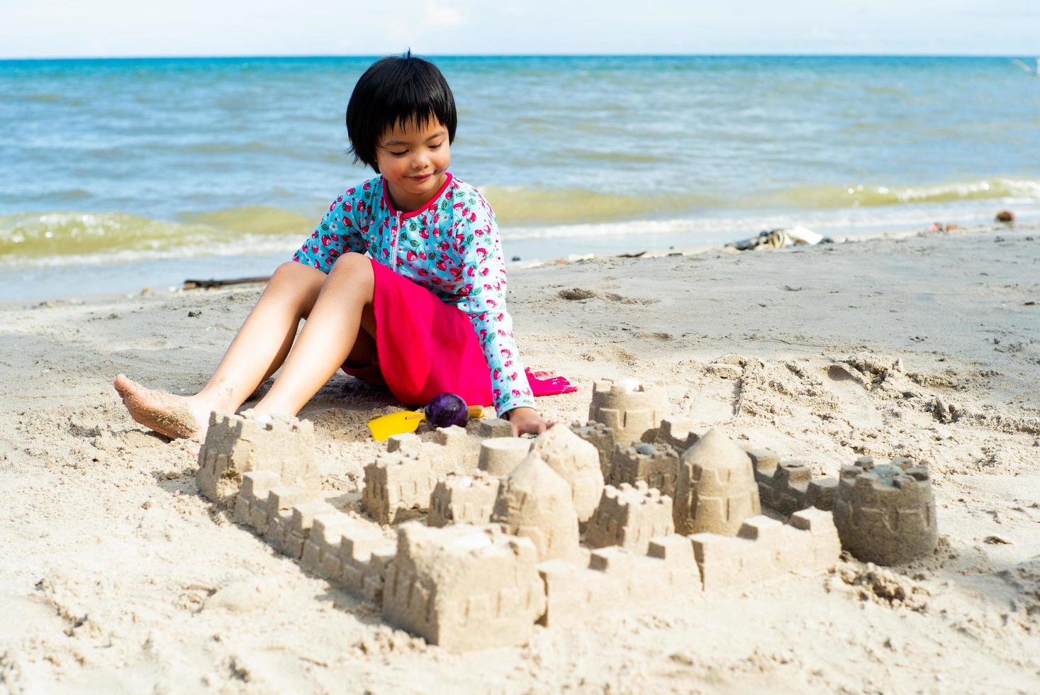 portrait de fille asain jouant dans le sable avec des jouets et la construction d'un château de sable. photo