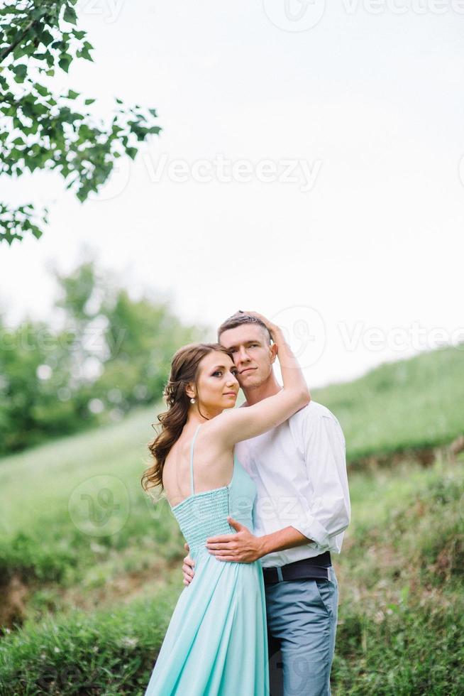 mec heureux dans une chemise blanche et une fille dans une robe turquoise se promènent dans le parc forestier photo