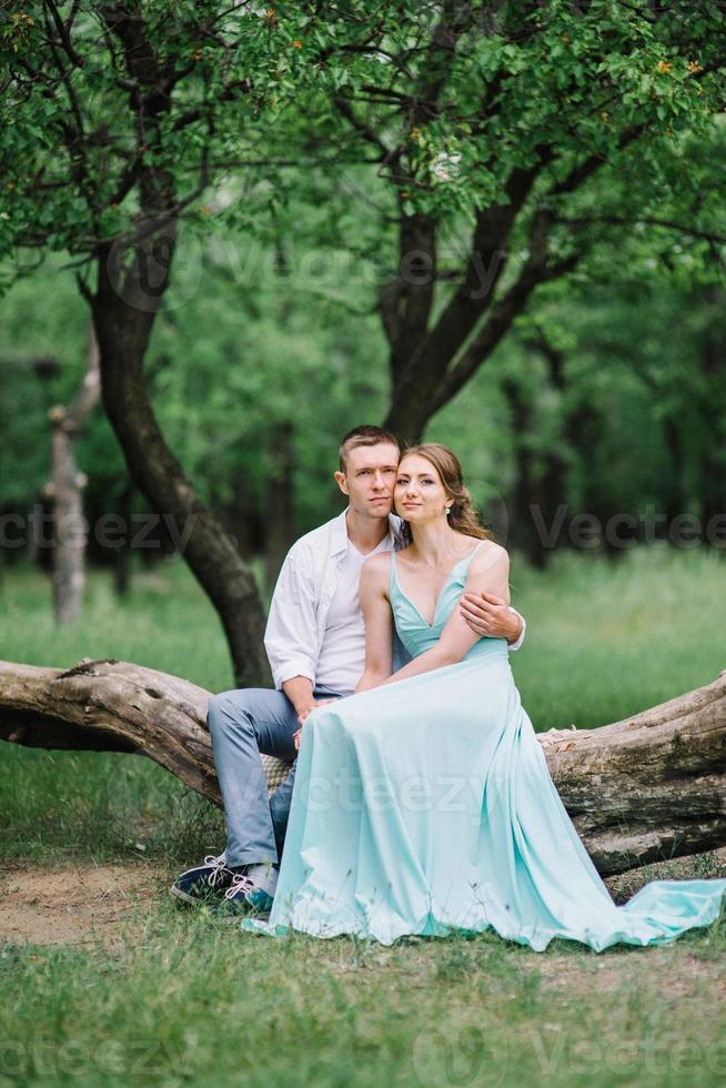 mec heureux dans une chemise blanche et une fille dans une robe turquoise se promènent dans le parc forestier photo