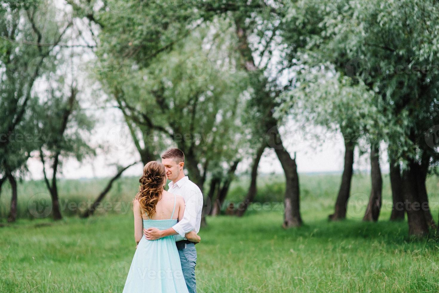 mec heureux dans une chemise blanche et une fille dans une robe turquoise se promènent dans le parc forestier photo