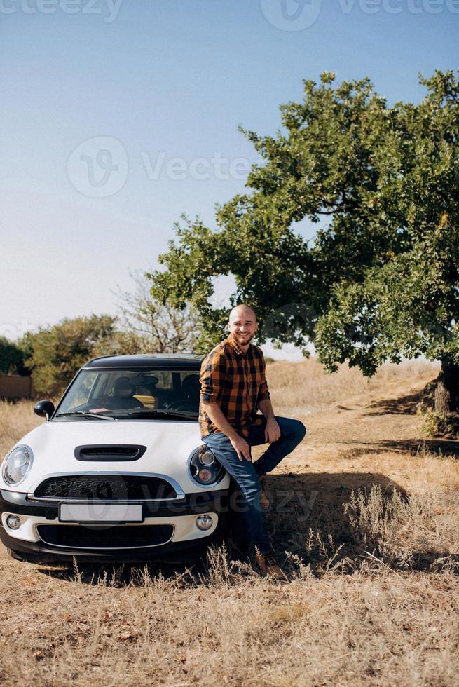 mec dans une chemise à carreaux à côté d'une voiture blanche photo