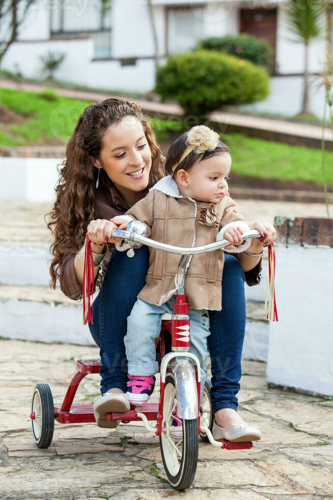 magnifique Jeune mère en jouant avec sa un année vieux bébé en plein air. avec maman équitation mon tricycle photo