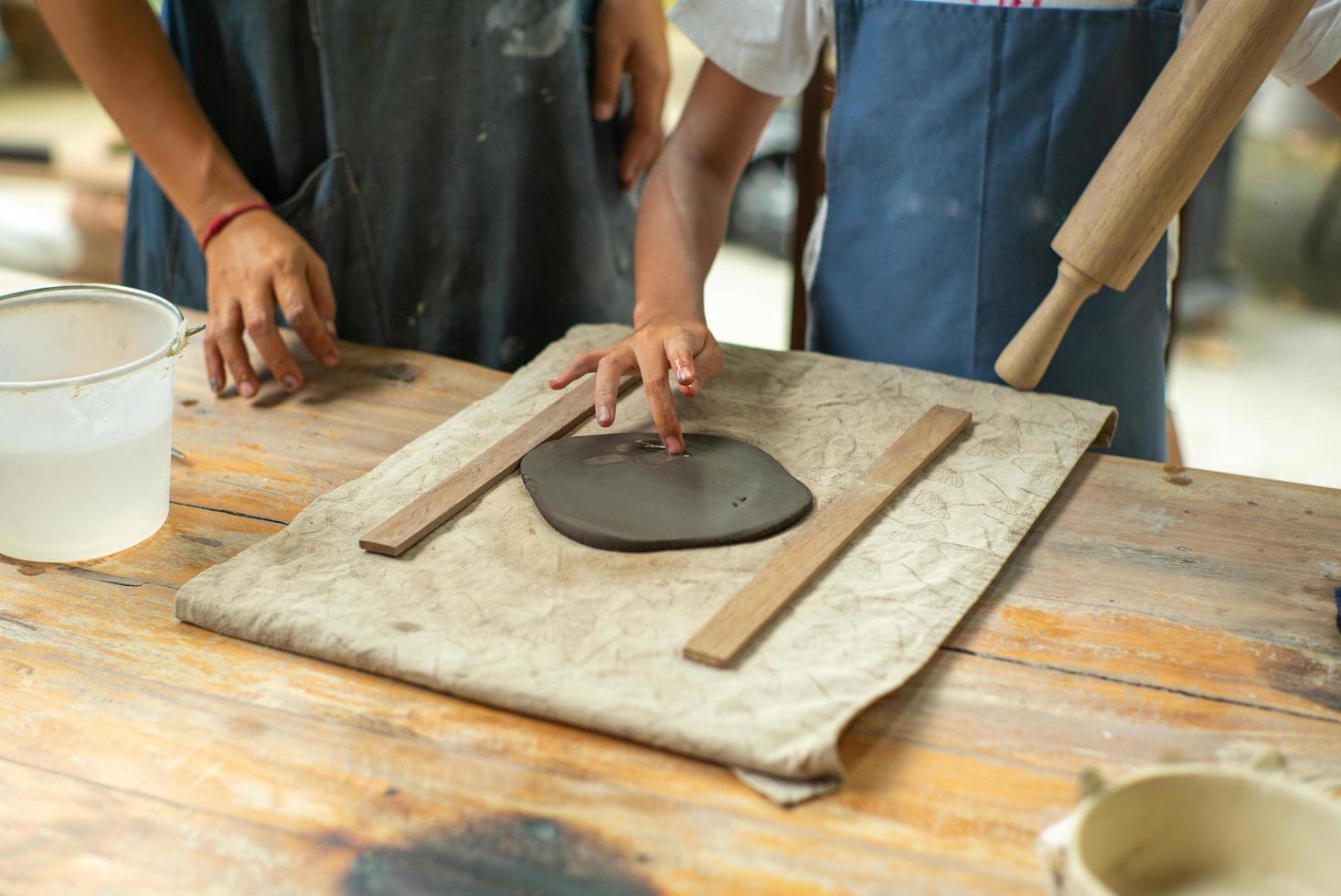 Gros plan des mains d'une fille à l'aide d'un rouleau à pâtisserie sur l'argile pendant la classe de l'atelier de moulage photo