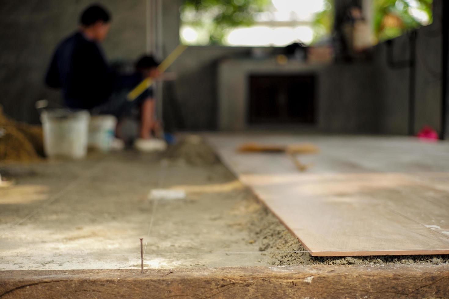 Carreaux de sol gros plan sur le ciment mixte avec du nylon pour le nivellement dans la maison en construction avec des travailleurs flous en arrière-plan photo