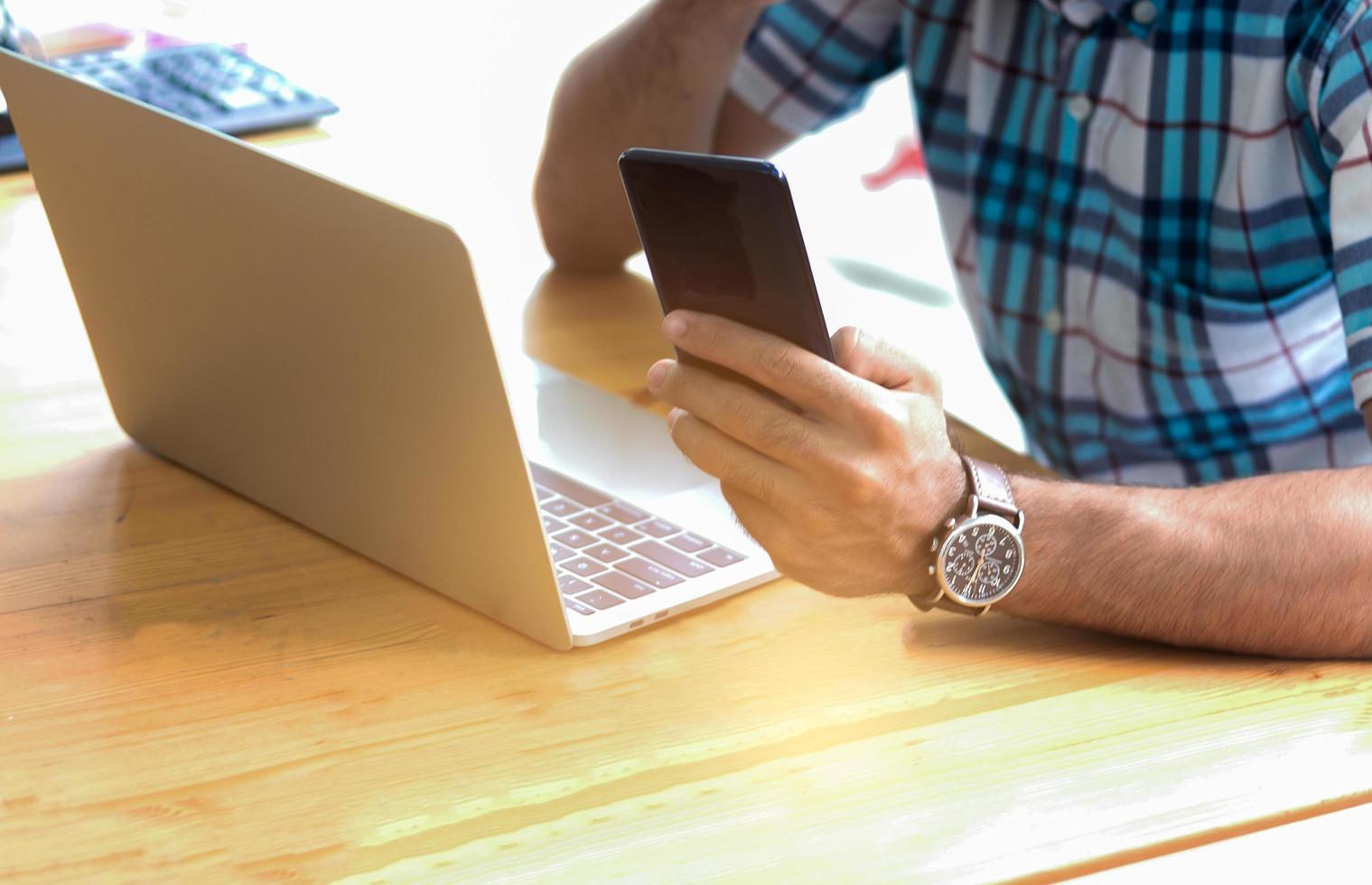 jeune homme d'affaires à l'aide d'un smartphone ou d'un téléphone portable et d'un ordinateur portable pour travailler à la maison en vacances. concept de travail et de faire des affaires en ligne photo