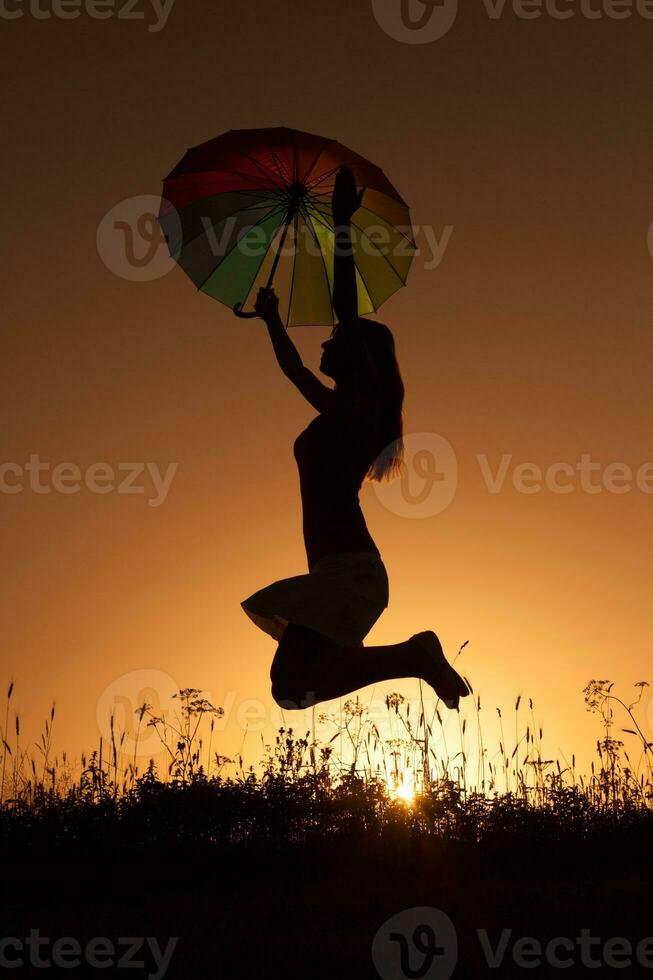 silhouette de une femme avec parapluie plus de le le coucher du soleil photo